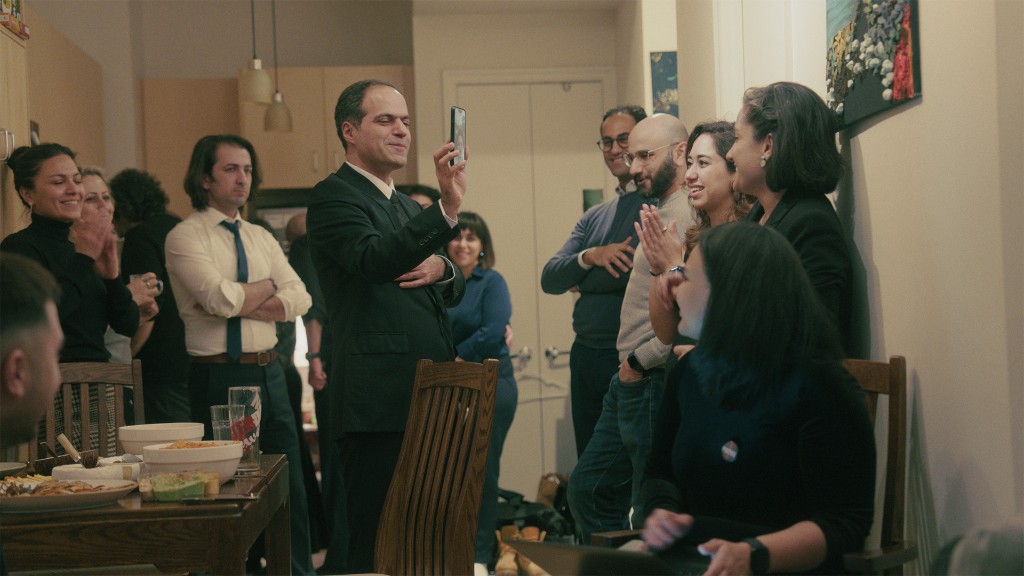 Family and friends gathered indoors, a man with his hand over his heart.