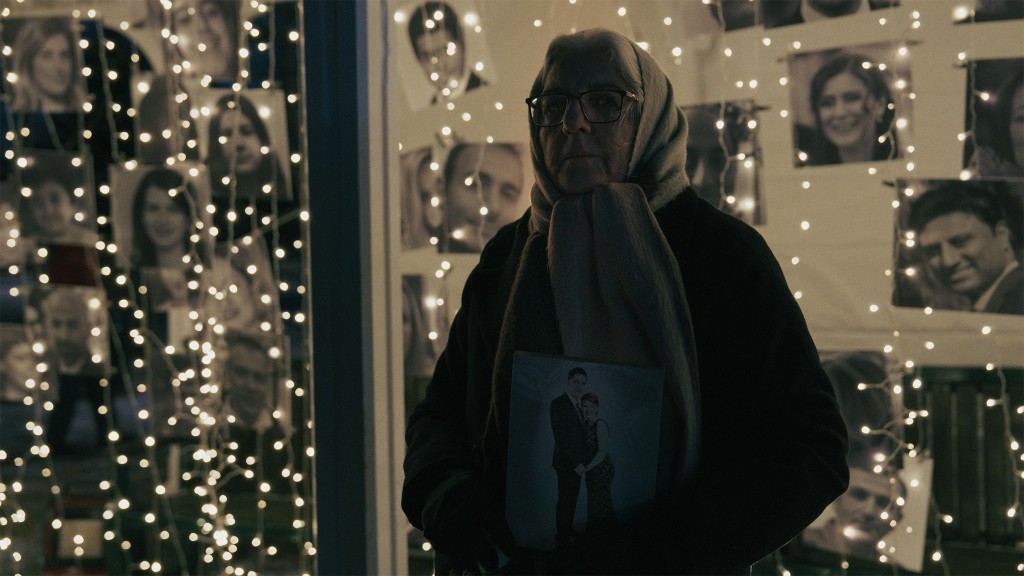 A woman holds a framed photograph at a memorial wall of portraits.