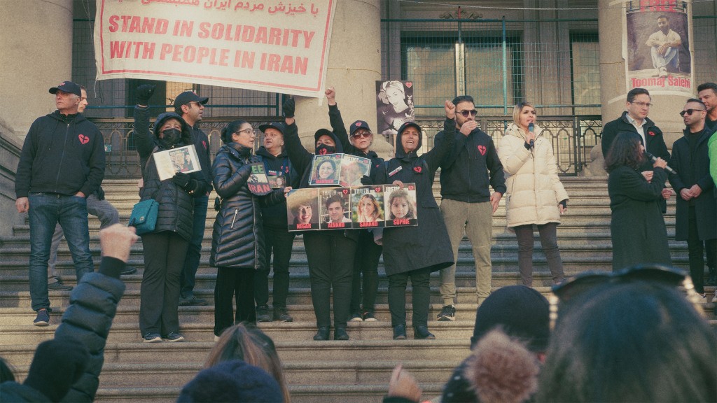 Advocates on the steps of a civic building, holding portraits and a banner in solidarity with people in Iran.